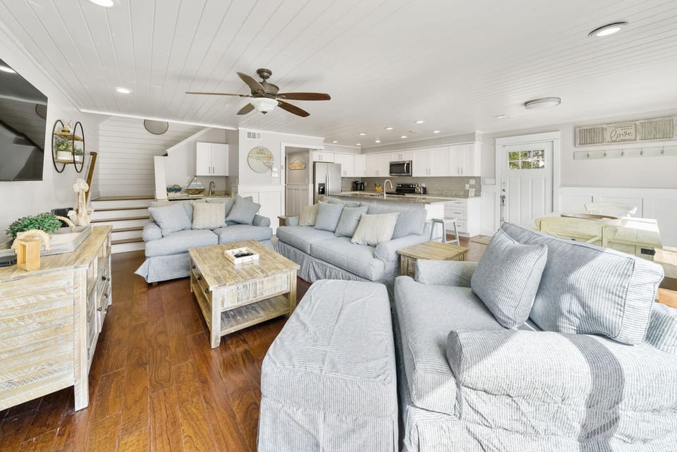 Relax in your spacious open-concept living area featuring comfortable seating, modern kitchen, and coastal charm throughout.