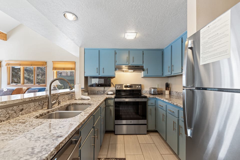 Your fully equipped kitchen features granite countertops, blue cabinetry, and stainless steel appliances, perfect for preparing home-cooked meals during your stay.