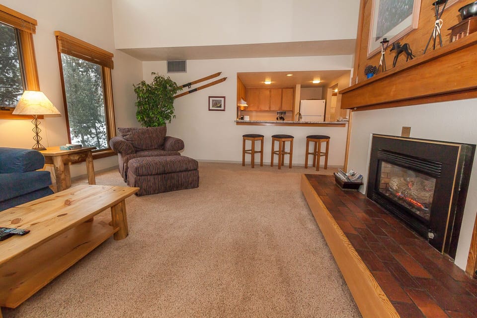 Unwind in your cozy living space with warm wood accents, a crackling fireplace, and an open kitchen perfect for preparing meals.