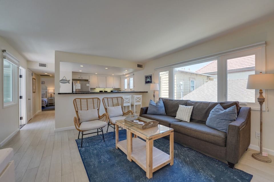 Relax in a comfortable living room complete with a sofa, wicker armchairs, a flat-screen TV, large windows for natural light, and coastal-themed artwork to set the beachy vibe.