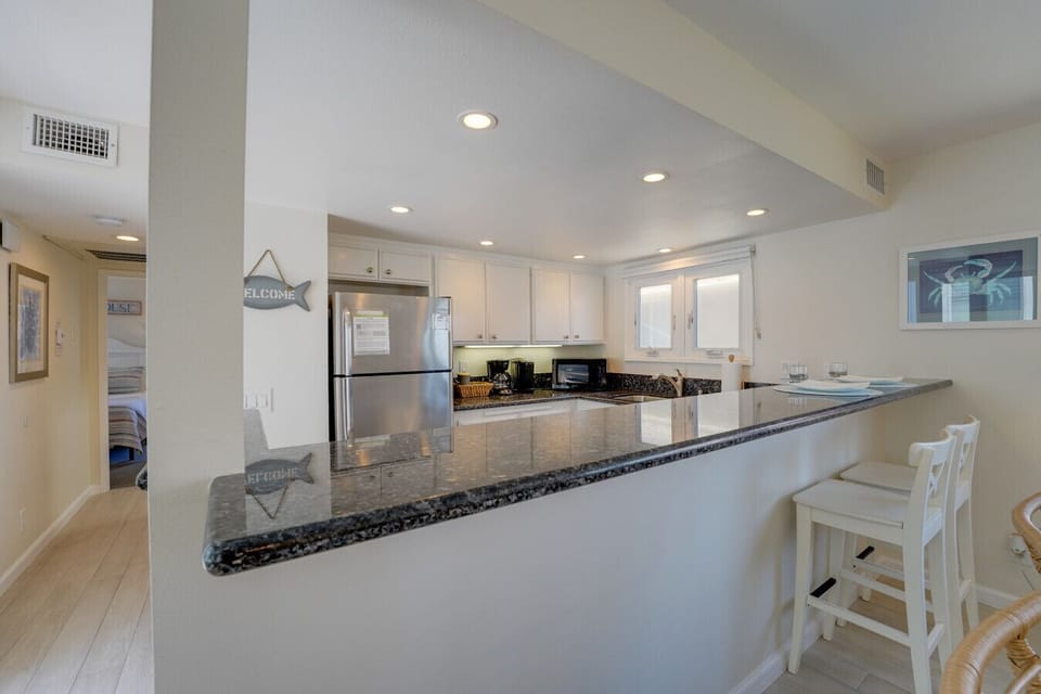 Bright and airy open-concept layout featuring a spacious living room, stylish wicker seating, bar seating at the granite breakfast counter, and a dining area with seating for six.