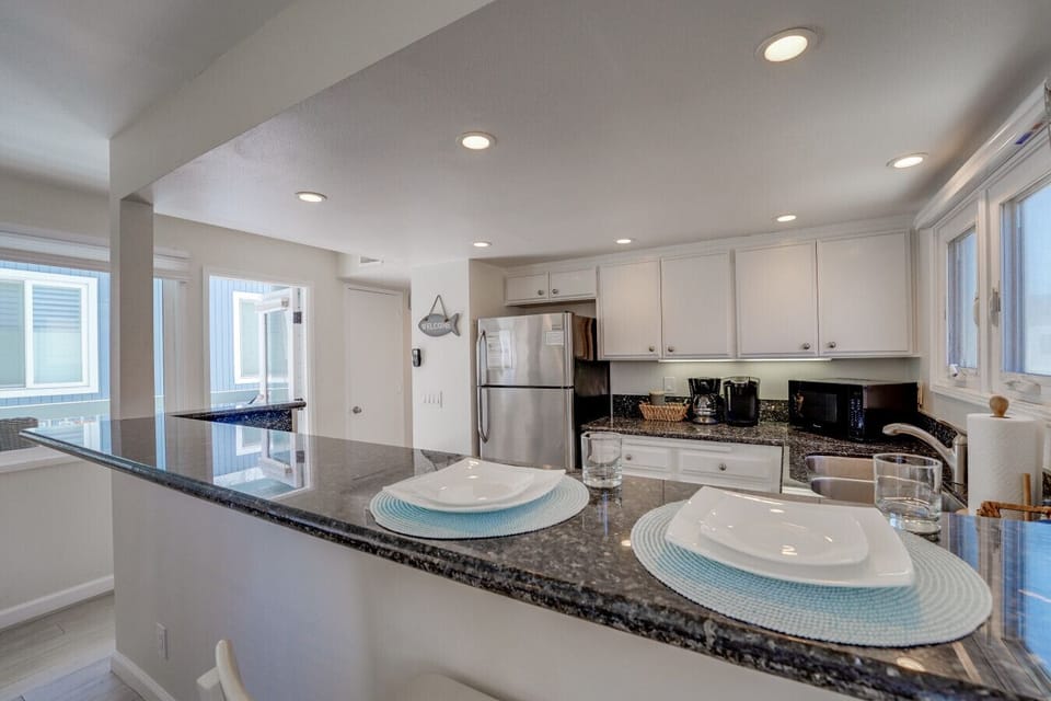 Bright and airy open-concept layout featuring a spacious living room, stylish wicker seating, bar seating at the granite breakfast counter, and a dining area with seating for six.