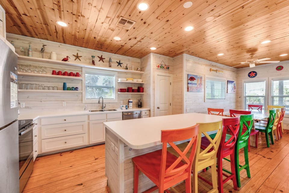 Your bright kitchen invites family meals with colorful seating, rustic wood ceiling, and open shelving for coastal charm.