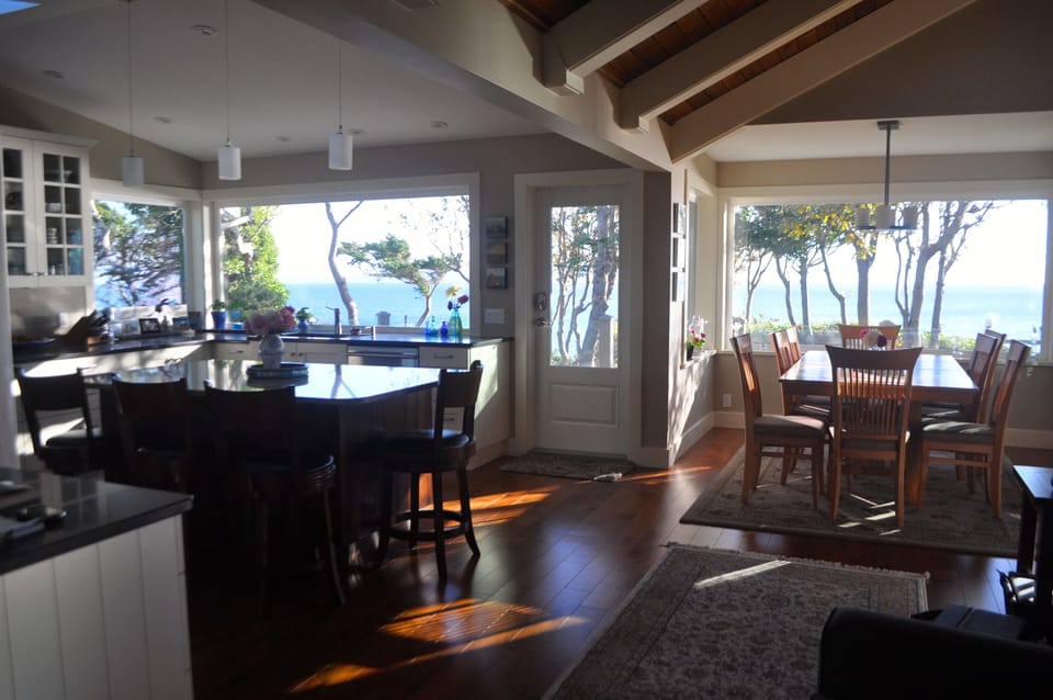 Dining room table surrounded by windows overlooking the ocean and front deck.