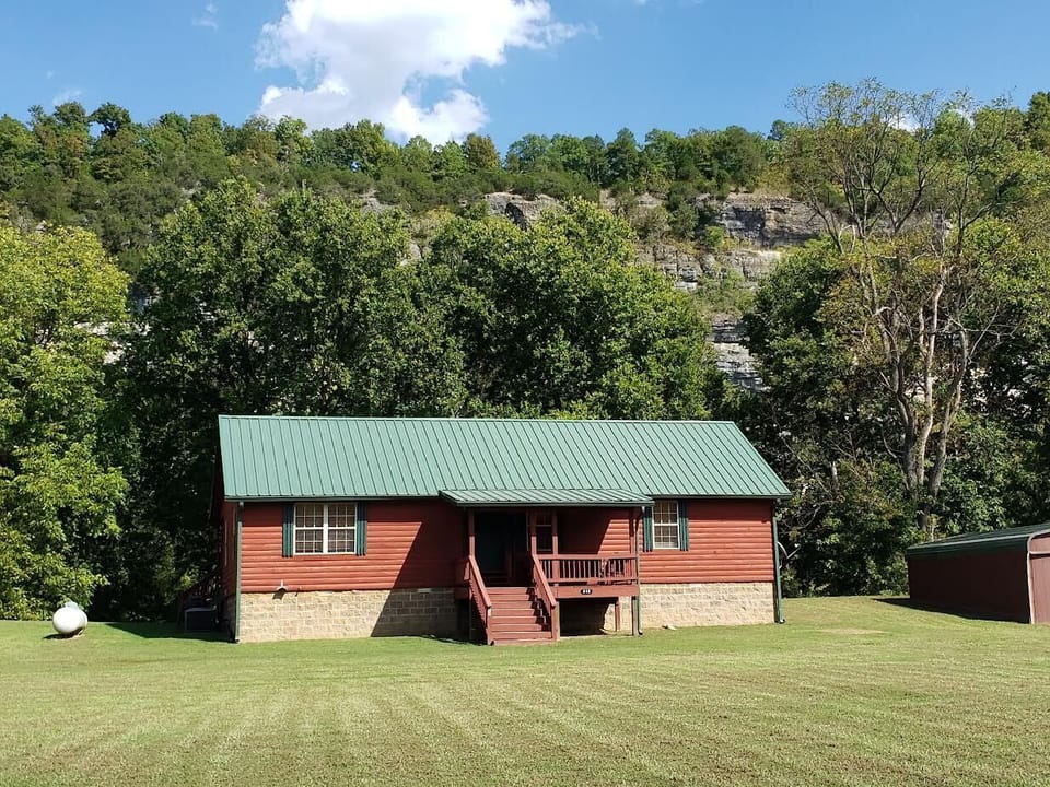 The river is between the cabin and the bluff behind the cabin.