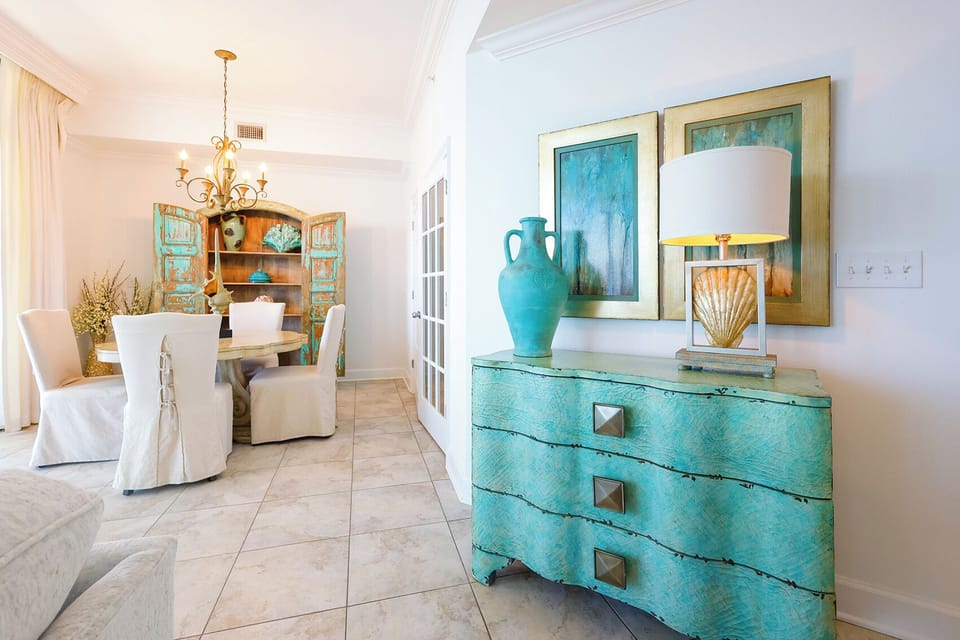Bright and inviting dining space featuring a turquoise cabinet, elegant chandelier, and cozy seating for memorable meals