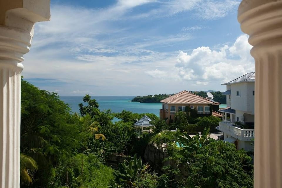 A picturesque balcony retreat offering serene sea views, accented by ornate pillars and a tapestry of tropical flora
