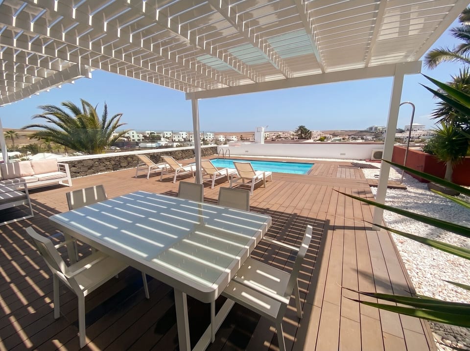 Al fresco dining: elegant glass table under the white pergola by the pool.
