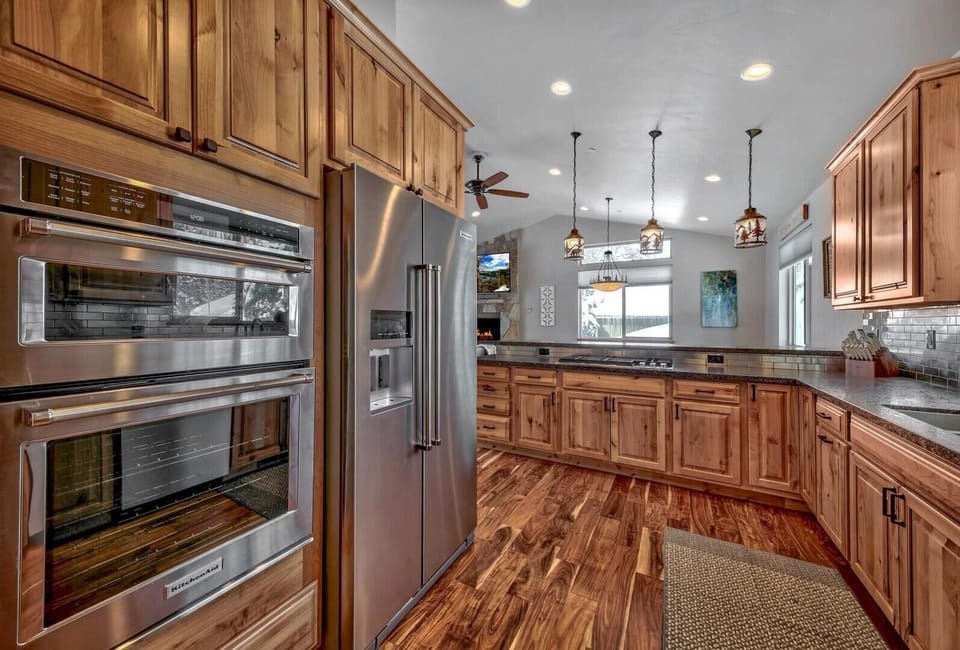 Stainless steel double oven and fridge stand beside knotty pine cabinets and a granite countertop in the kitchen.