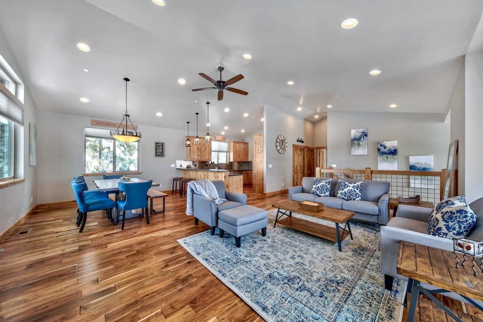 Open living and dining area with hardwood floors, blue upholstered chairs, vaulted ceilings, and natural wood cabinetry.
