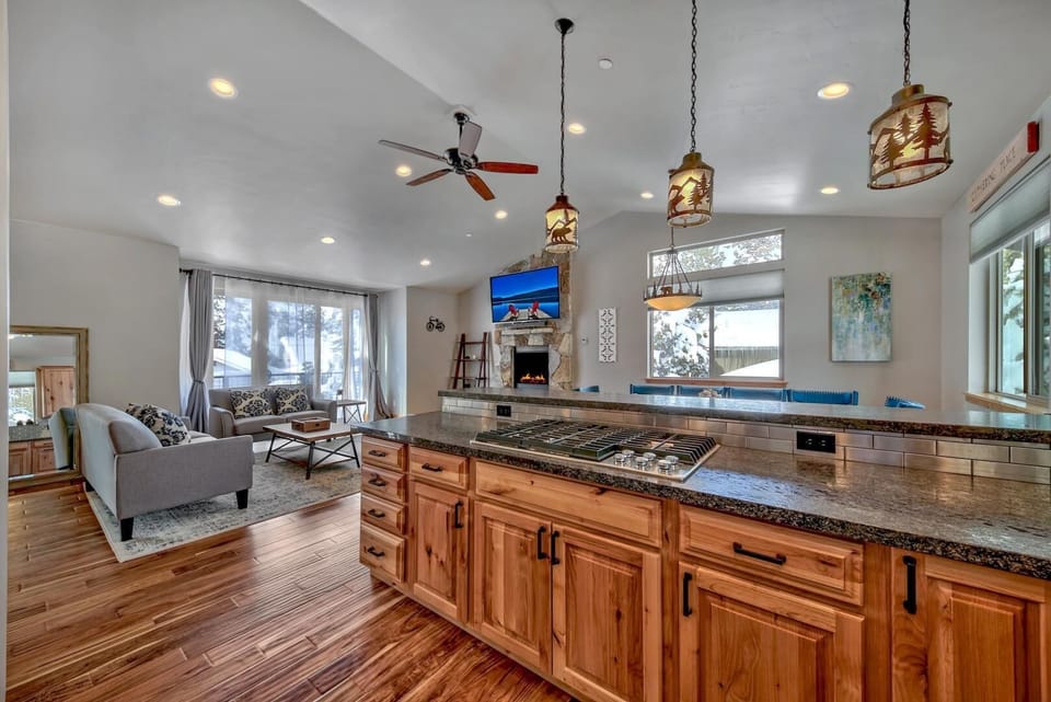 Granite countertop island with gas cooktop overlooks living area with stone fireplace and sliding glass doors.