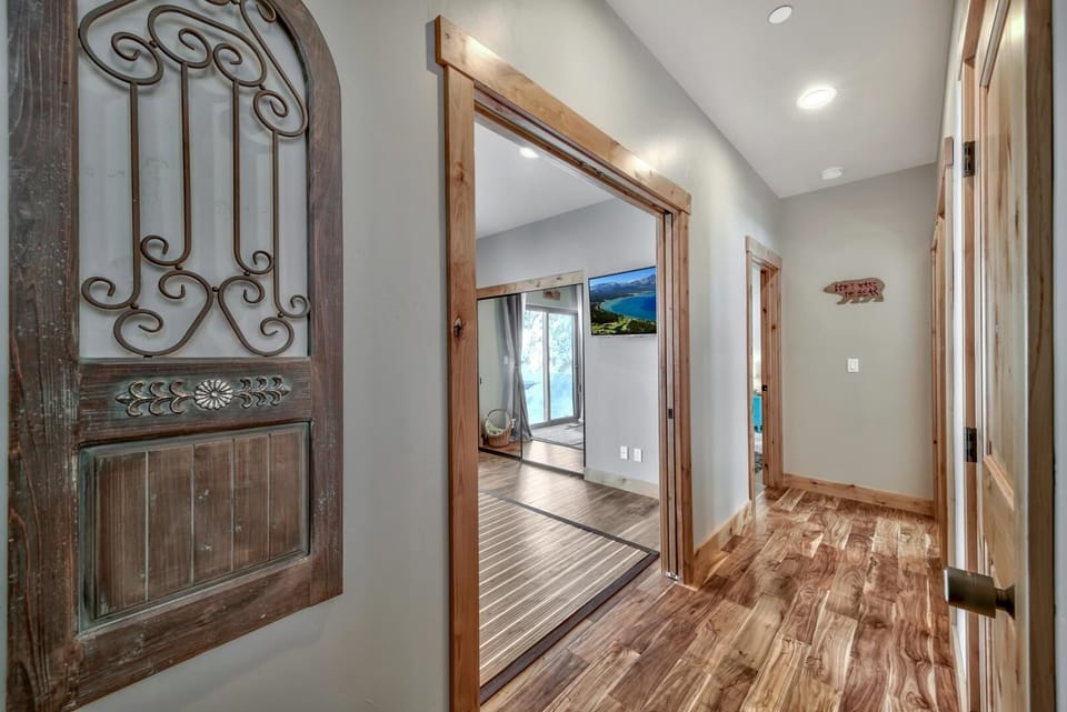 Hallway with glossy wood floors, natural wood trim, and a decorative wrought-iron wall panel near bedroom entrances.