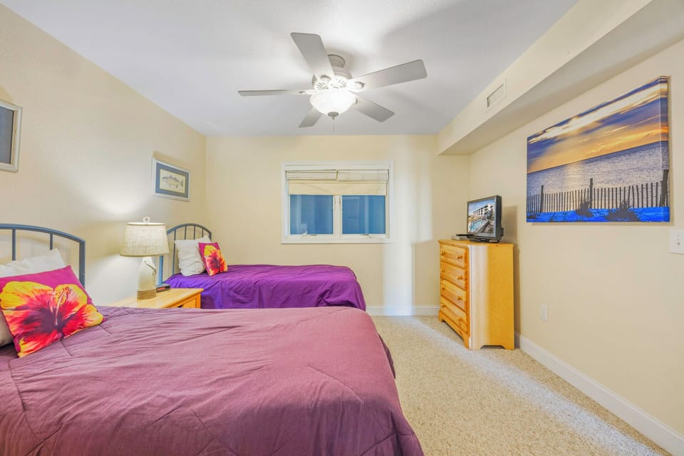 Relax in your coastal-themed bedroom featuring two comfortable beds, gentle ceiling fan, and beautiful beach artwork that sets the perfect vacation mood.