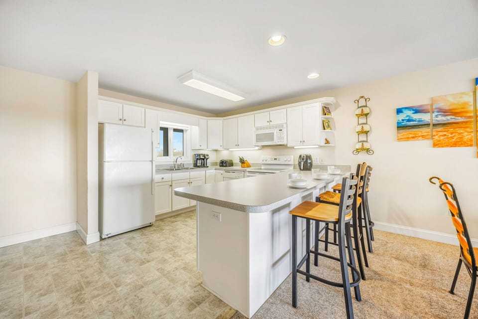 Cook your favorite meals in this bright, fully-equipped kitchen featuring modern appliances, spacious counters, and a breakfast bar perfect for morning coffee.