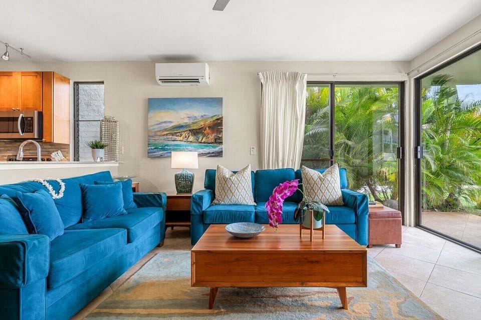 Indoors, teal sofas and coastal art gather light, sliding doors opening the room to greenery.