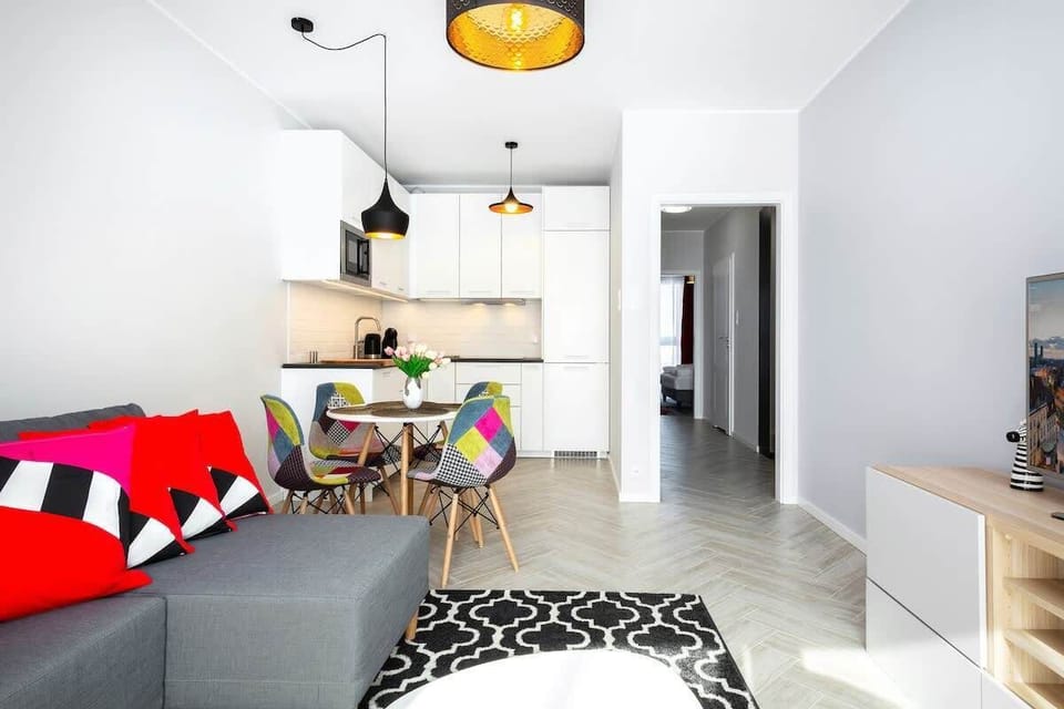  Another view of the living room with additional seating, a dining area, and the same colorful decor as in the first living room photo. The overall look is bright and inviting.

