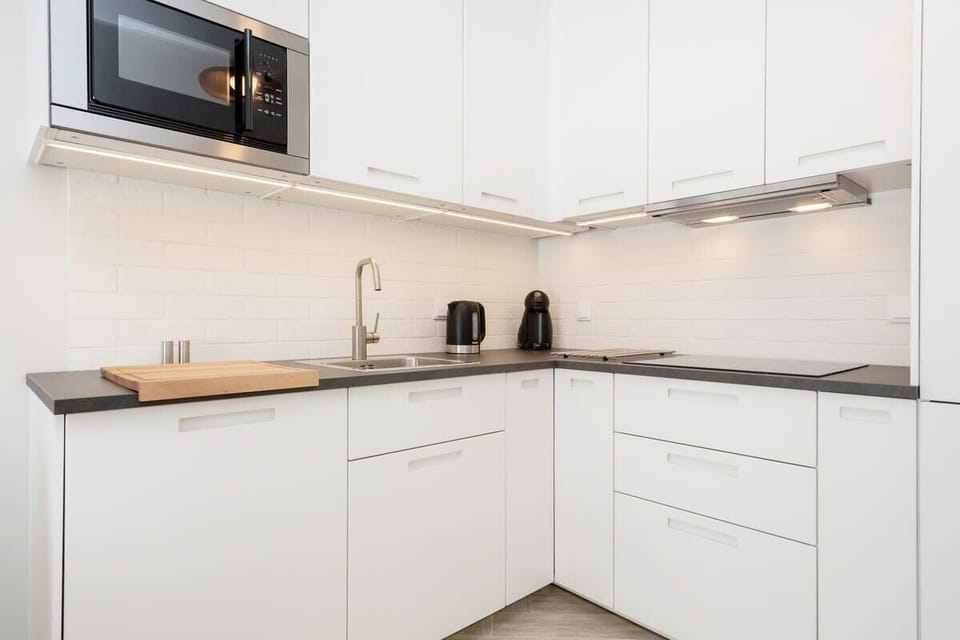 A modern kitchen with white cabinets and clean lines. There are a few appliances on the countertop, such as a  kettle.