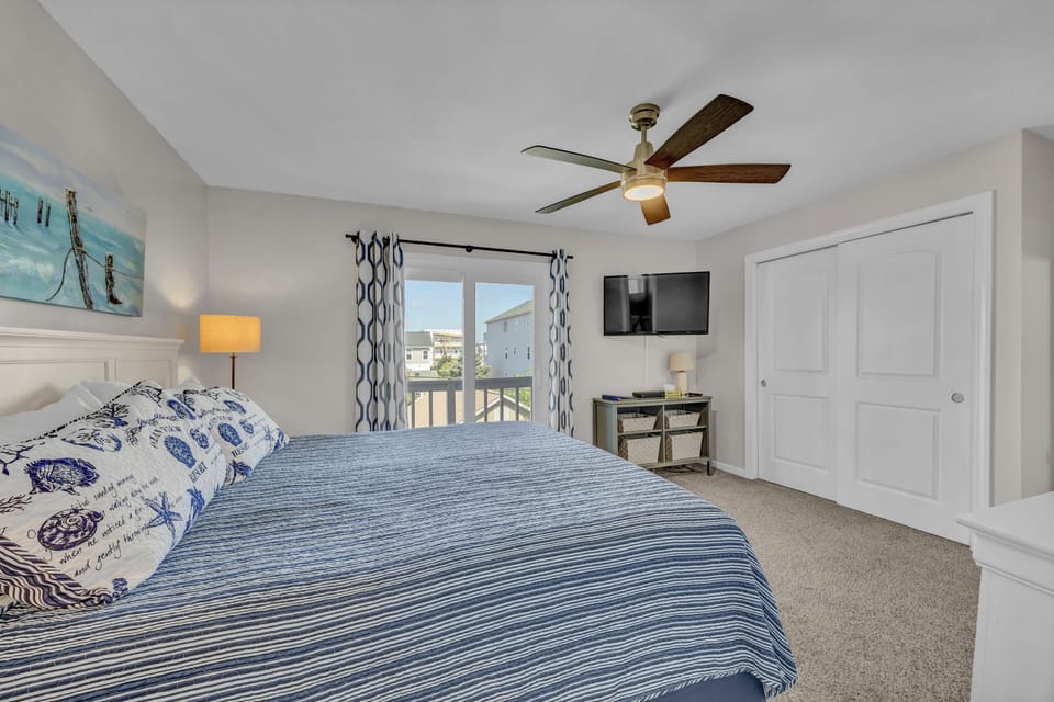 Sink into crisp linens in your serene bedroom with coastal touches, a ceiling fan overhead, and glimpses of the neighborhood beyond your window.