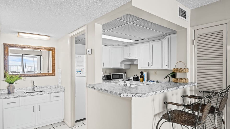 Gulf Tower 1C - Studio-style condo featuring a vanity area and a fully equipped kitchen with a breakfast bar and two high chairs.