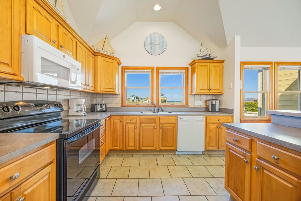 Your spacious kitchen features warm wood cabinets and ocean views through large windows, perfect for preparing meals while watching the waves.