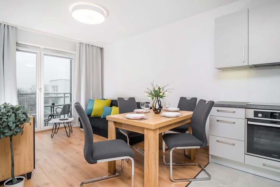 A bright living room with a light wood floor, cozy gray sofa, and large windows, creating an open and airy ambiance.
