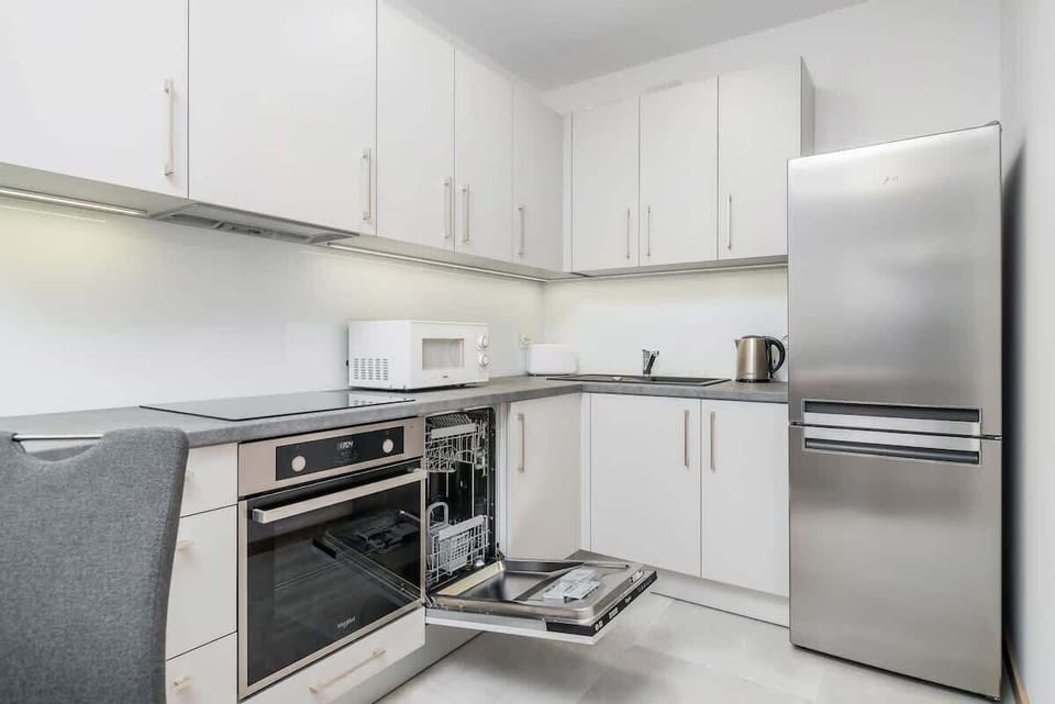 A sleek kitchen featuring white cabinetry, stainless steel appliances, and an organized countertop, offering a clean and functional cooking area.