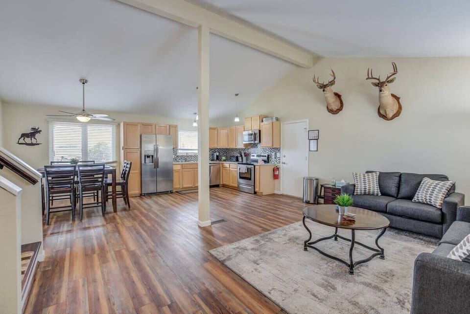 Open living area with wood-style floors, a soft rug, and comfortable seating flowing into the dining table and kitchen—an easy space to gather, chat, or relax on the couch while still being part of everything happening around you.