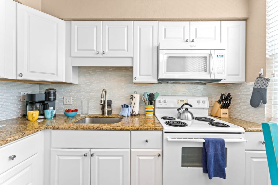 Fully equipped kitchen with fridge, oven, stove, microwave, and Keurig coffee maker, flowing into a cozy living and dining space.