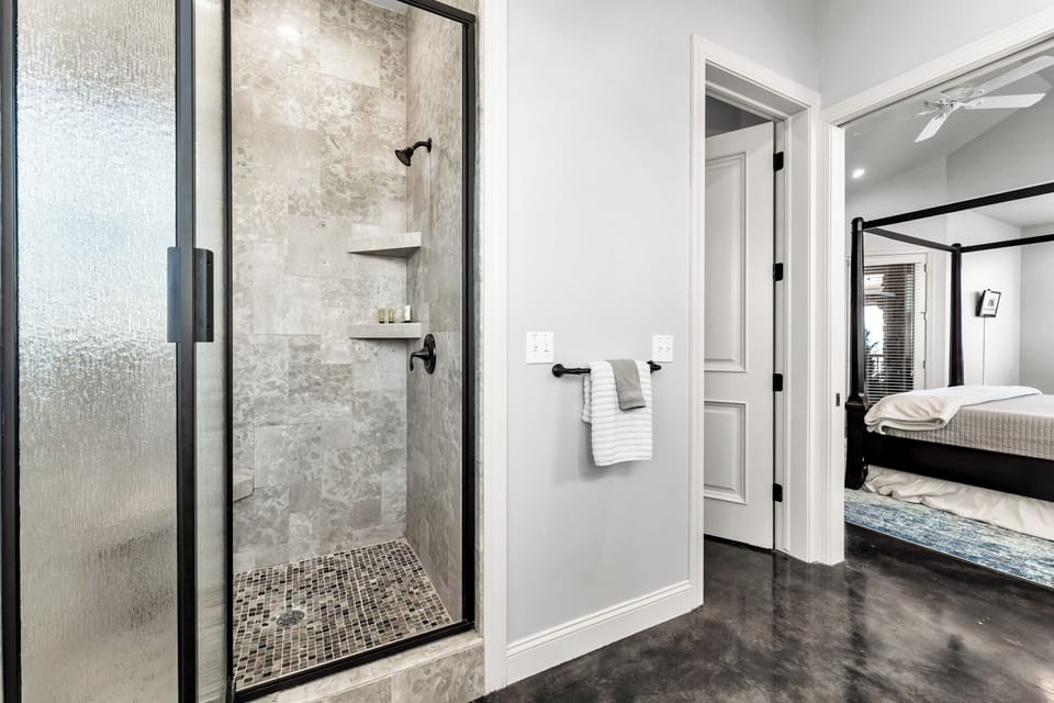 Walk-in shower in master bath looking into master bedroom with king bed.