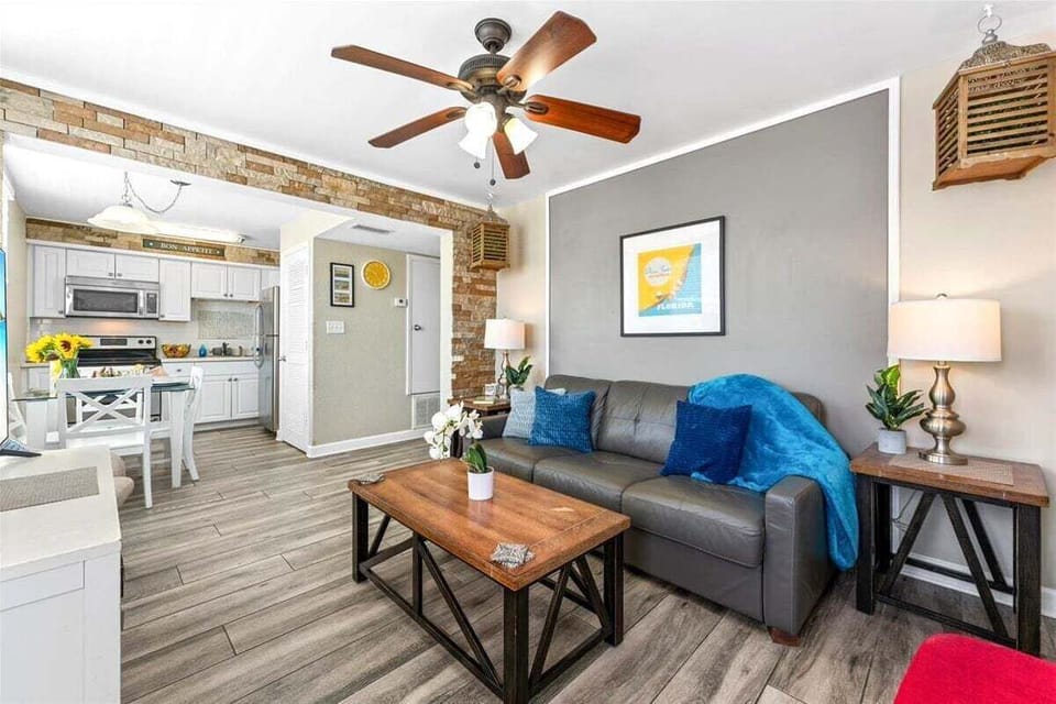 Living room area with a sofa bed, 2 single chairs, smart TV, and ceiling fan.
