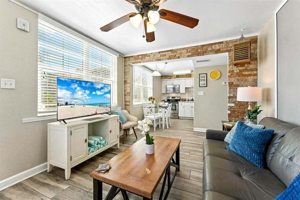 Living room area with a sofa bed, 2 single chairs, smart TV, and ceiling fan.