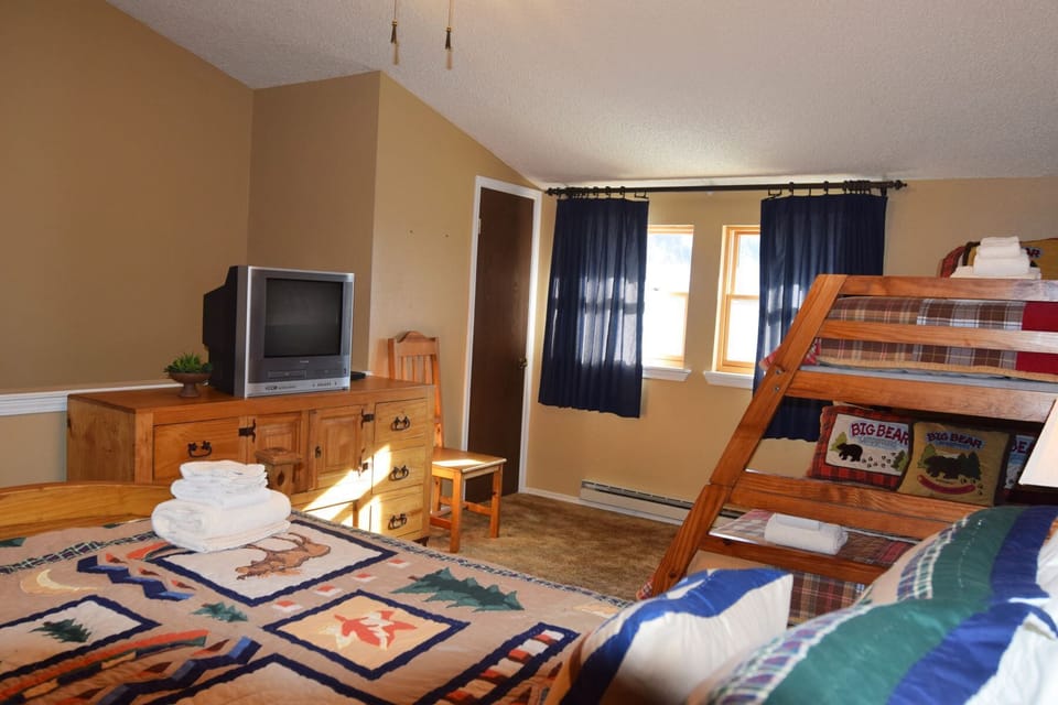 Your family room features a bunk bed for kids and a queen bed, all set up with fresh towels and rustic wooden furniture. Natural light fills the space where everyone can unwind together.