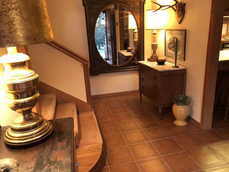 As guests enter, the entry hall mirror reflects the grounds' pines and creek.