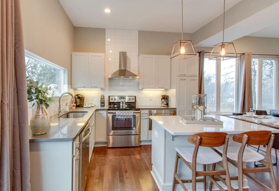 A clean white kitchen with stainless appliances and a large window is bright and fully stocked for cooking.