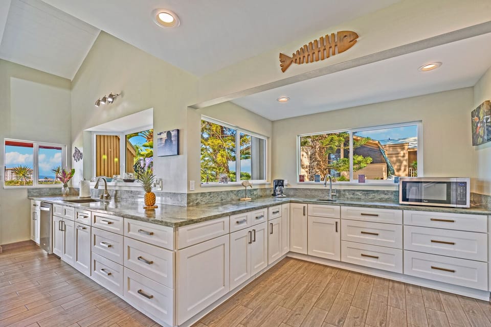 Fully equipped modern kitchen with panoramic windows, offering plenty of natural light and views of tropical landscaping.