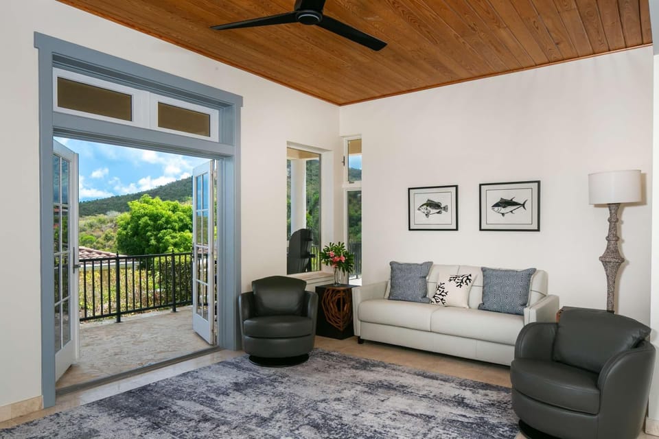 Living room with leather swivel chairs, white sofa, fish prints, and open French doors to a stone balcony.