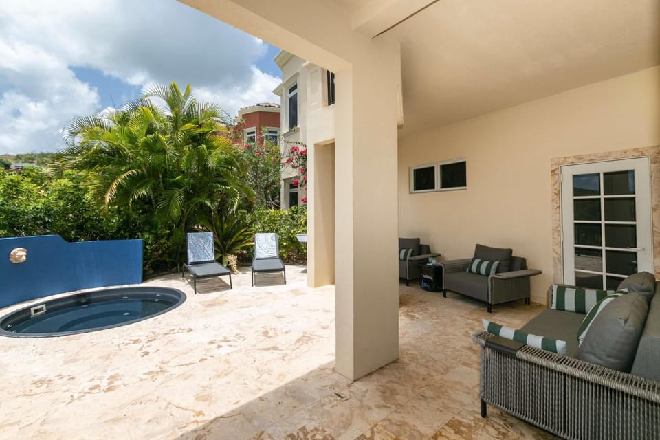 Covered patio with woven wicker sofas featuring striped cushions and a marble tile floor extending to outdoor loungers.