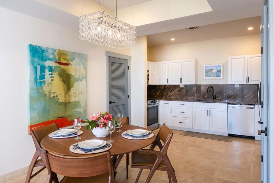 Dining area features a round wood table set with plates and glasses beneath a glass bubble chandelier.