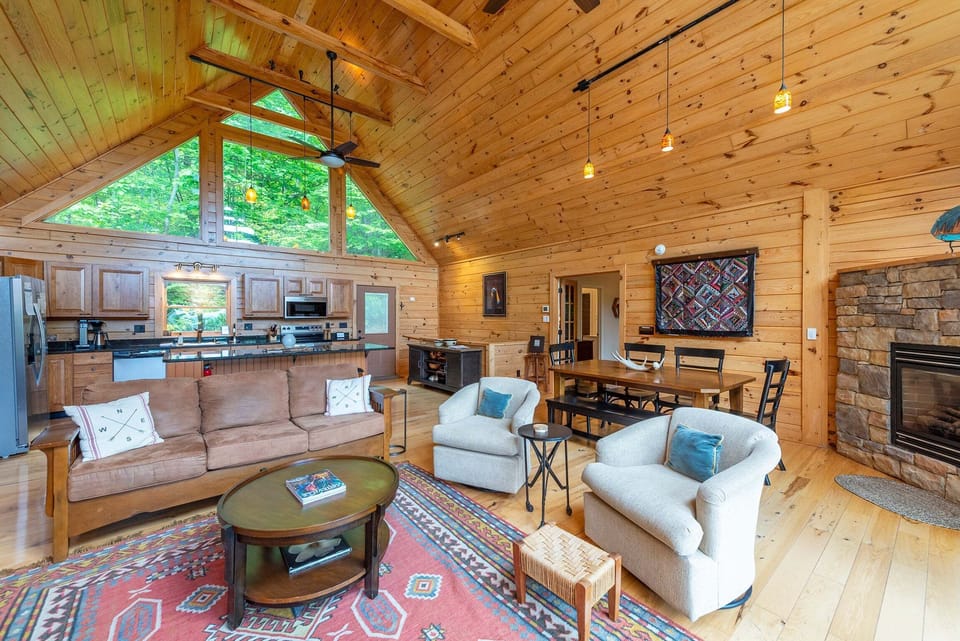 Spacious great room with soaring vaulted ceilings, a stone fireplace, and large windows that flood the space with natural light, creating a warm and inviting atmosphere.