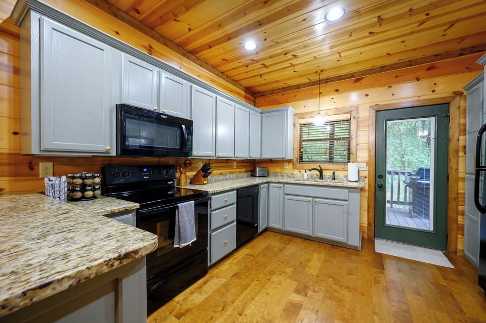 Your fully-equipped kitchen features modern appliances, granite countertops, and warm wood-paneled walls—perfect for preparing meals while enjoying the cozy cabin atmosphere.