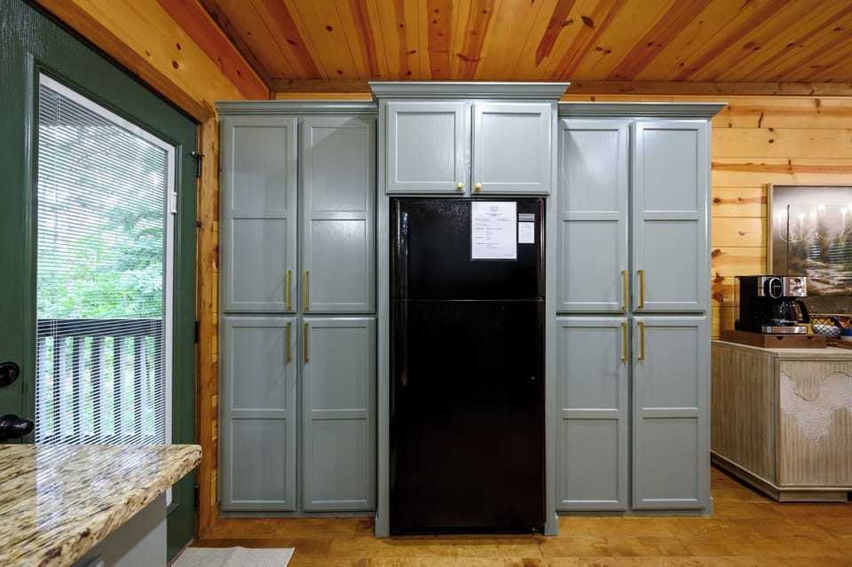 Your fully-equipped kitchen features elegant grey cabinetry, ample storage, and modern appliances beneath warm pine ceiling beams. Store groceries and prepare meals with ease as natural light fills the space.