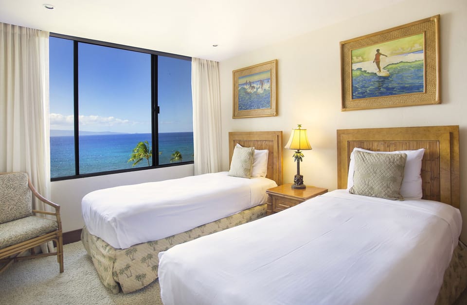 Wake up to breathtaking ocean views framed by floor-to-ceiling windows. Two plush beds invite restful nights, while tropical artwork and warm wood accents create your perfect island retreat.