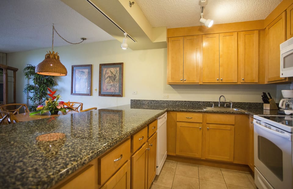Your fully-equipped kitchen features warm wood cabinetry, granite countertops, and everything you need to prepare meals during your stay. Natural light and tropical accents create a welcoming atmosphere.