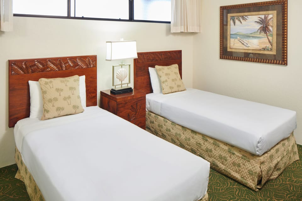 Your tropical retreat awaits with two plush twin beds dressed in crisp white linens and beach-inspired accents. Wake to natural light streaming through large windows as island artwork sets the vacation mood.