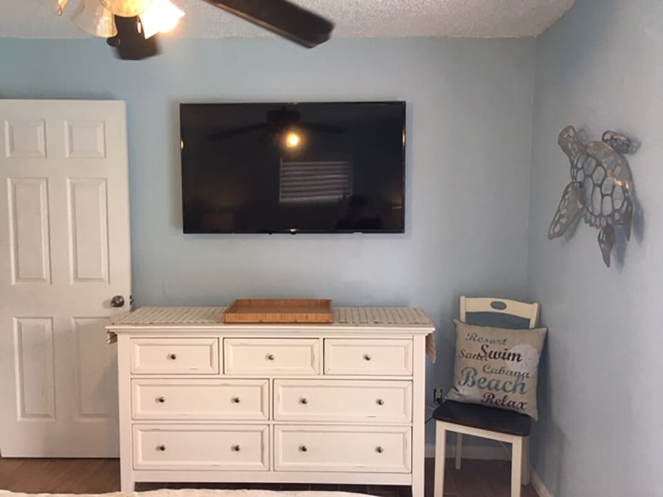 Large flat screen, sea turtle art work, dresser and chair master bedroom