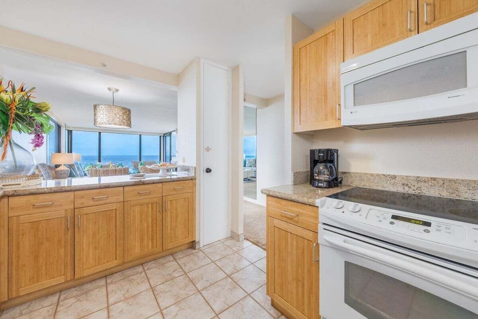 Enjoy cooking in this airy kitchen with warm tones, sleek finishes, and ocean views in the background