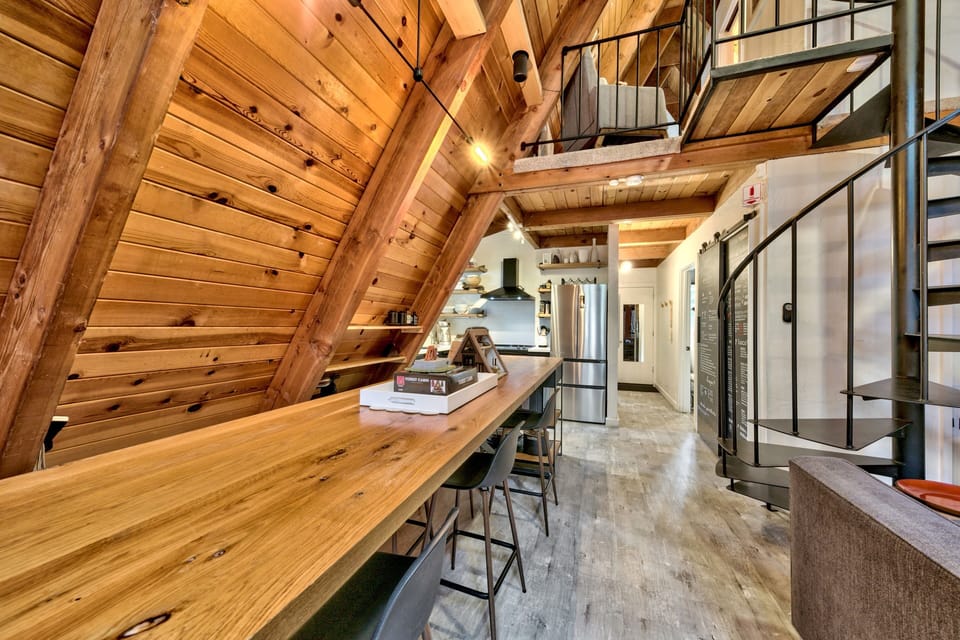 Step into your stunning loft-style retreat where soaring timber ceilings create dramatic warmth above your fully-equipped kitchen and modern steel staircase.