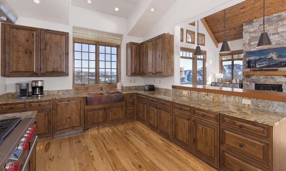 Your gourmet kitchen features rich wood cabinetry, granite countertops, and mountain views through expansive windows—perfect for preparing meals while enjoying the scenery.