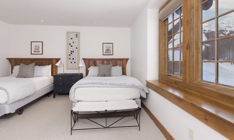 Wake up to stunning mountain views through expansive windows in your cozy twin bedroom, where rustic wood meets crisp white linens.