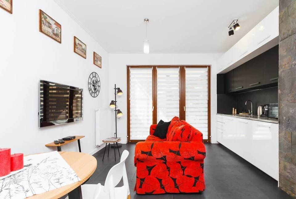  A stylish living room with a striking red sofa, white walls, and a large window that enhances the airy atmosphere.